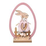 Figurina decor pentru masa de Paste, forma de ou roz, iepuras imbracat in haina cu blanita, cu oua colorate, floricele de primavara, iarba si gard, pe stativ din lemn, inaltime 16.5 cm